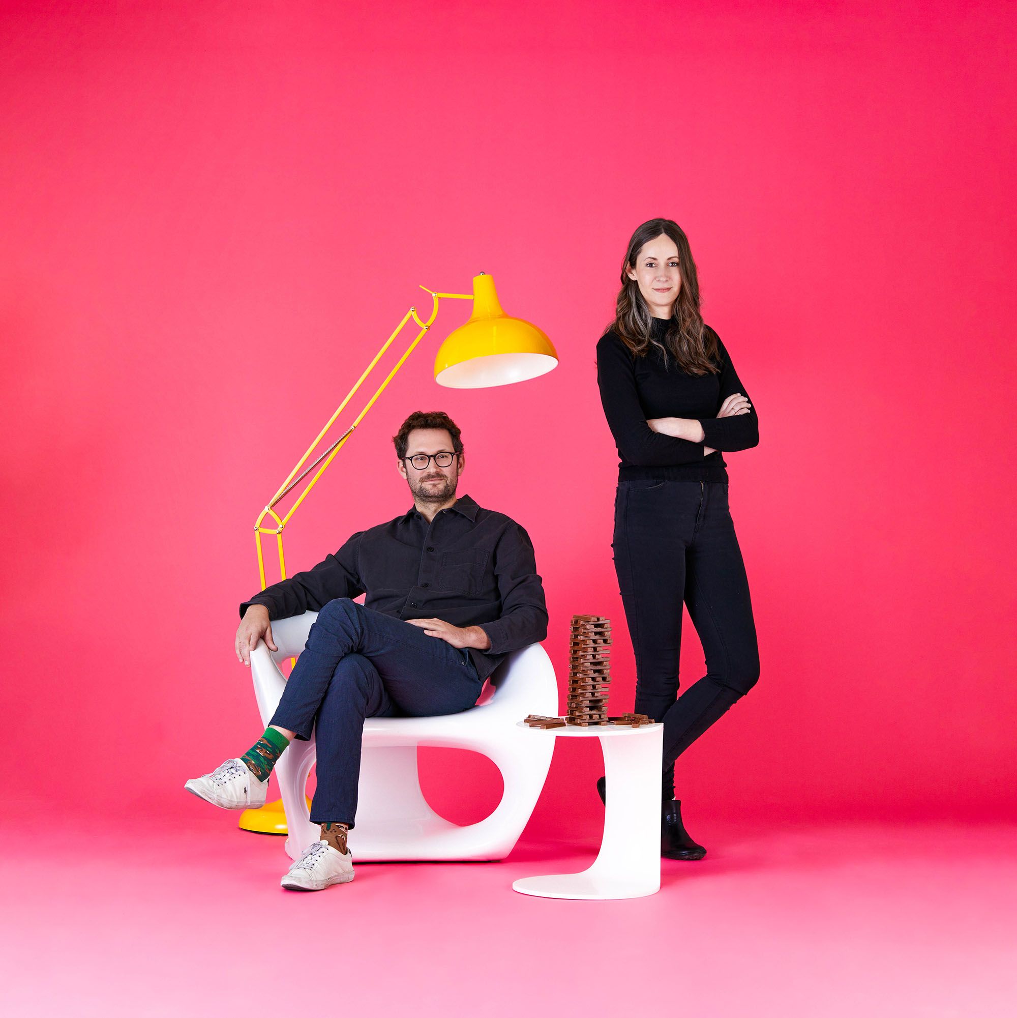 Man sitting and woman standing in front of a pink background